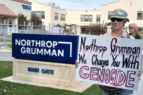 At main entrance holding sign "Northrup Grumman we charge you with genocide"
