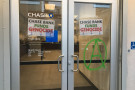 the front entrance to a chase bank with large plate glass doors. the doors have signs that read 'chase bank funds genocide'