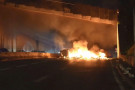 Multiple lanes of a highway are blocked by a burning barricade.