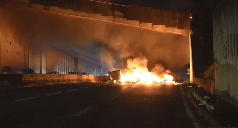 Multiple lanes of a highway are blocked by a burning barricade.