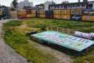 A colorful, painted wooden platform in People's Park, surrounded by a fence made of shipping containers.