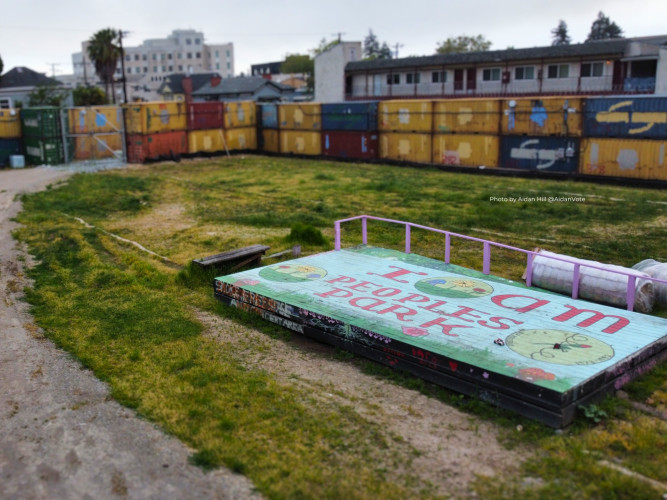 A colorful, painted wooden platform in People's Park, surrounded by a fence made of shipping containers.